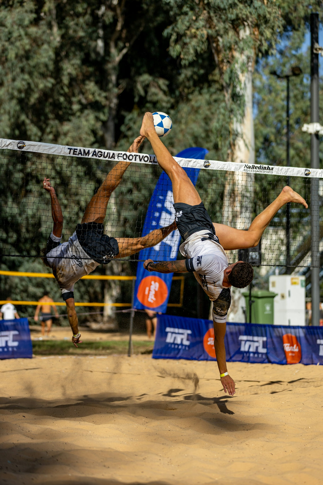 Two athletes playing footvolley on a sandy court