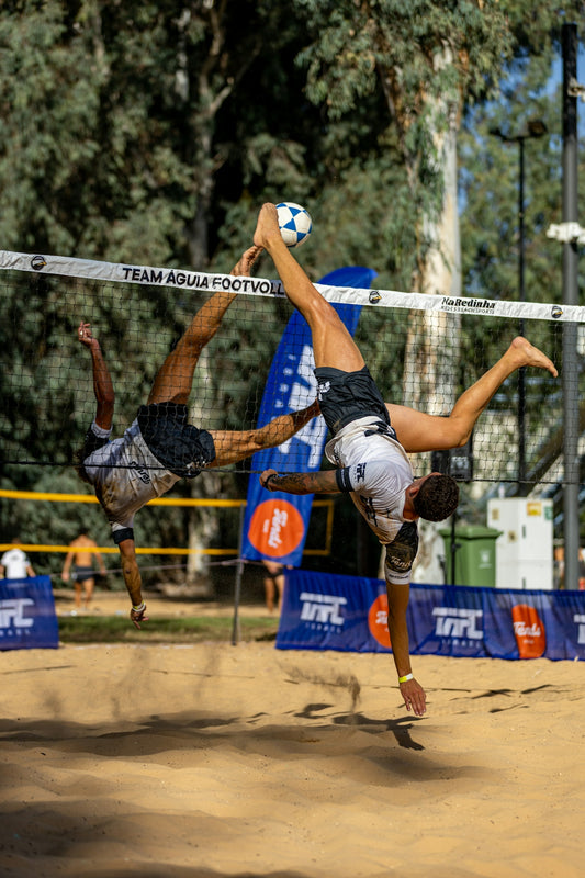 Two athletes playing footvolley on a sandy court